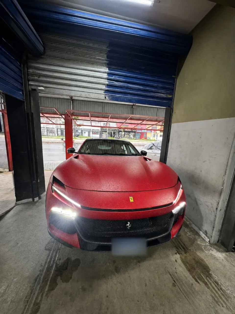 Ferrari Purosangue vermelha fosca na entrada da oficina da RM, com os faróis acesos