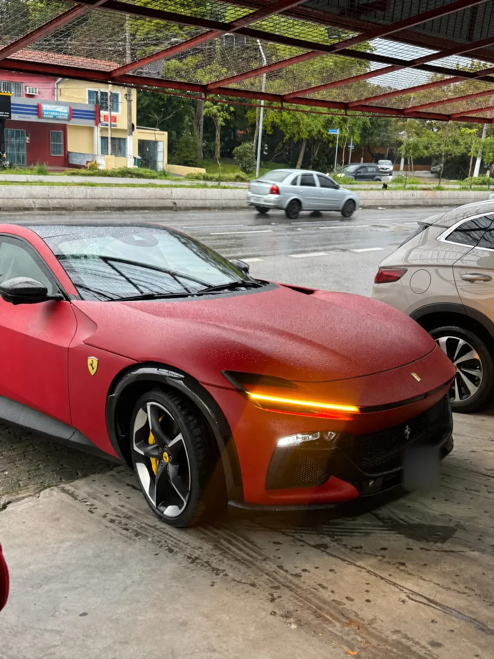 Ferrari Purosangue vermelha fosca com o farol aceso, na entrada da RM